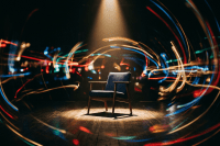 Empty cushioned chair under spotlight on wooden floor with colorful light trails swirling around